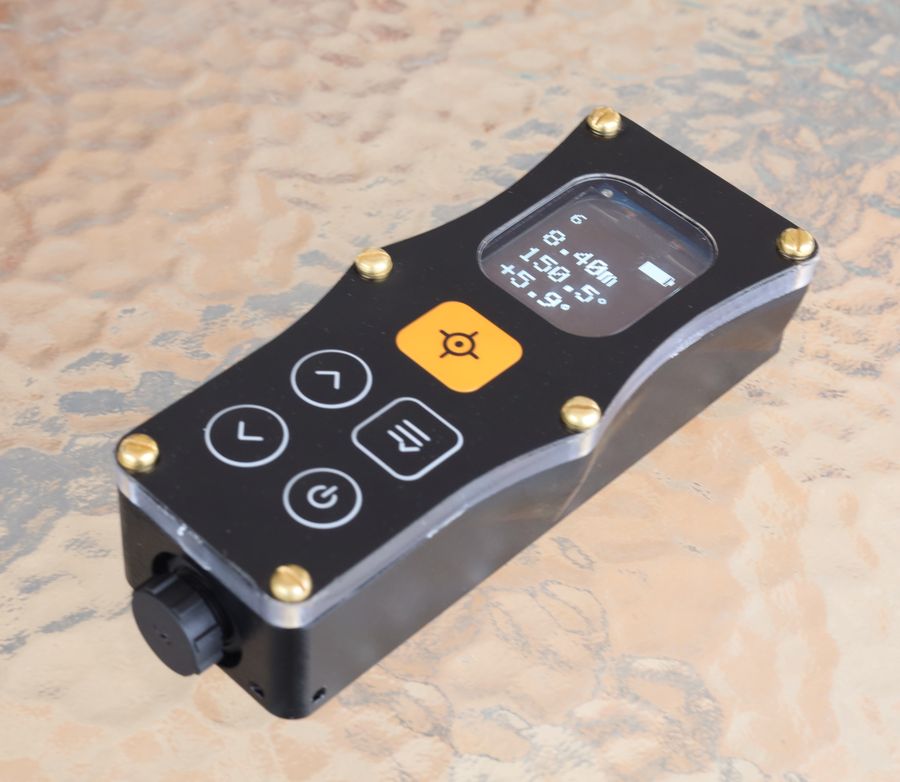 Three-quarter view of the assembled DiscoX, showing the orange shot button, the four-button keypad, the brass corner fixings and a display reading 8.40 m, 150.5 degrees and plus 5.9 degrees.
