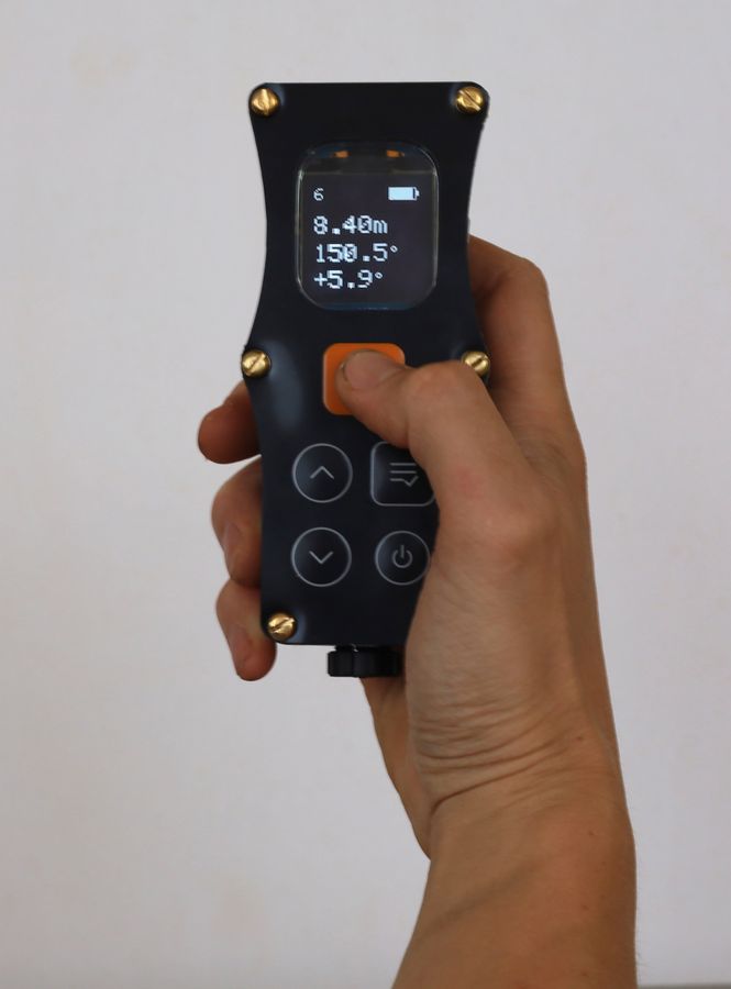 The DiscoX held upright in one hand with the thumb resting on the orange shot button and the lit display facing the camera.