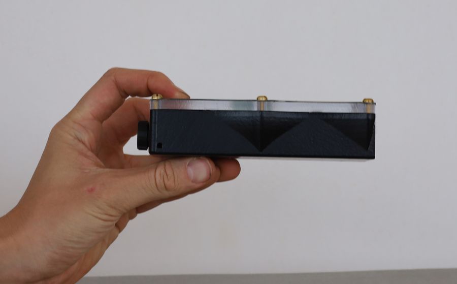 The DiscoX held side on, showing the faceted underside of the printed case below the clear top plate.
